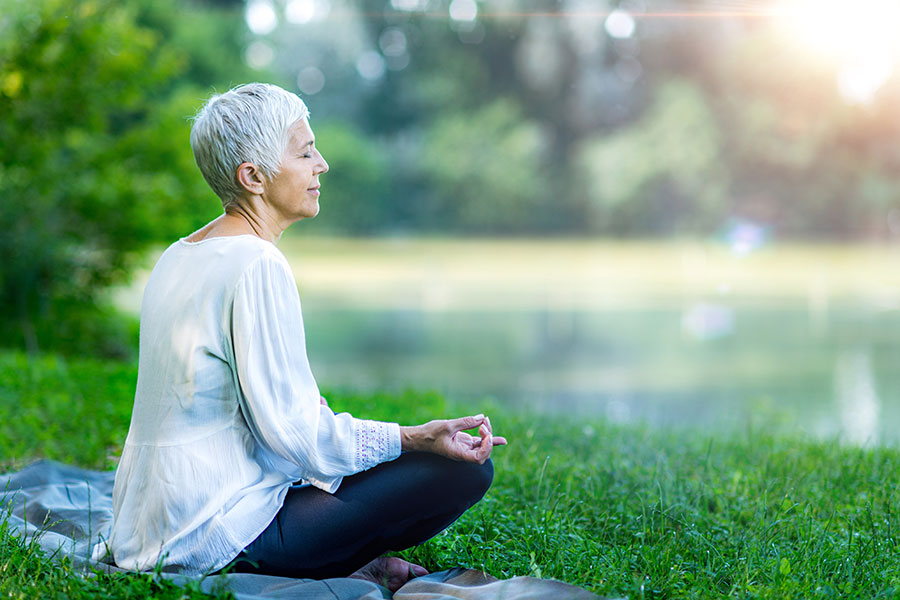 senior woman meditating by the water in nature